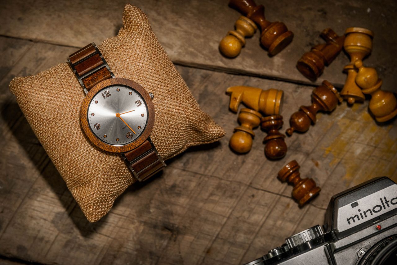 Home Vintage wooden wristwatch on burlap pillow beside scattered chess pieces and Minolta camera on rustic table.