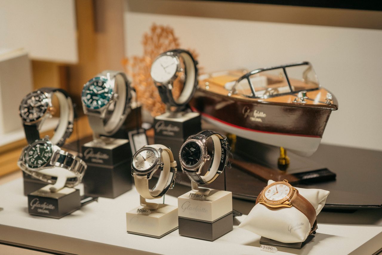 Home A collection of luxury watches elegantly displayed beside a model boat in a retail environment.